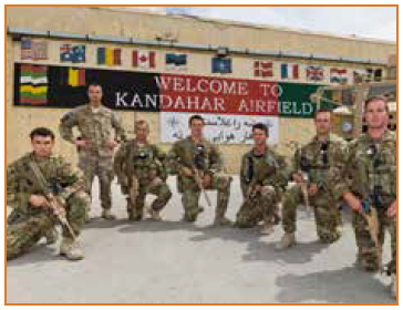 Photo of seven soldiers in front of a sign that reads 'Welcome to Kandahar Airfield'